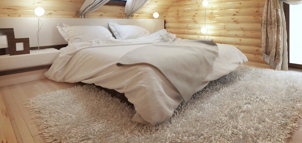 Bedroom interior in a log on the attic floor with a roof window. Large bedroom with bedside tables and a shaggy carpet. Bedroom in modern style. 