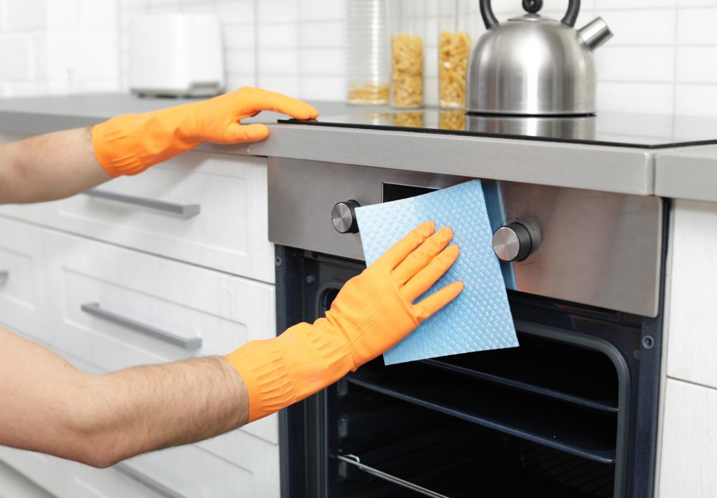 Young man cleaning oven with rag in kitchen, closeup