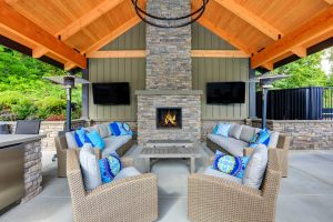 Inviting interior of covered patio area in Tacoma Lawn Tennis Club. Stone fireplace wicker furniture with beige cushions and bright blue pillows. Northwest USA